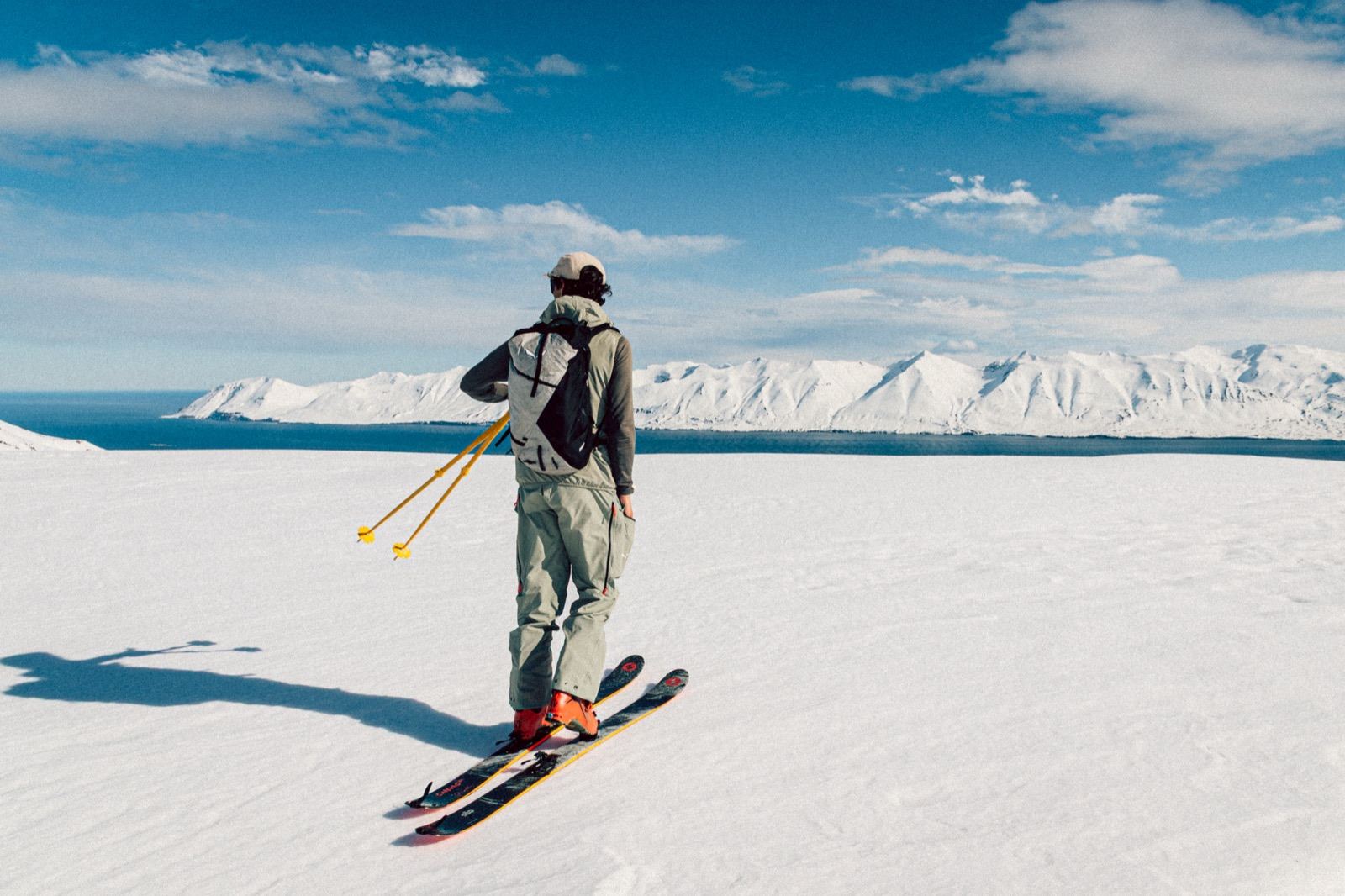 Sciatore di spalle guarda il fiordo dalla cima innevata, Islanda
