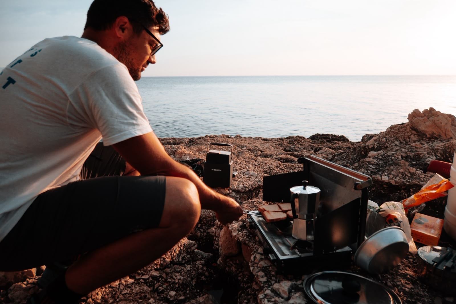 Cena al fornello da campo sulle rocce, il mare al tramonto dietro